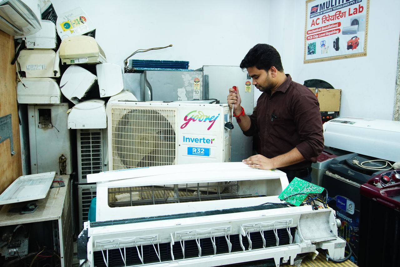 our-experience Technician repairing an air conditioner unit in New Delhi workshop.